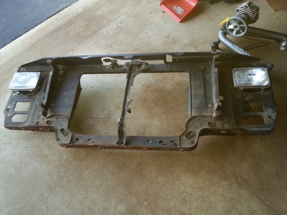 Black metal radiator support assembly with headlights attached.