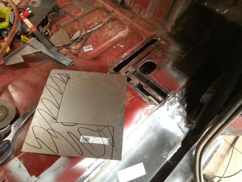 Sheet metal with markings on a rusted vehicle floor, with tools in the background.
