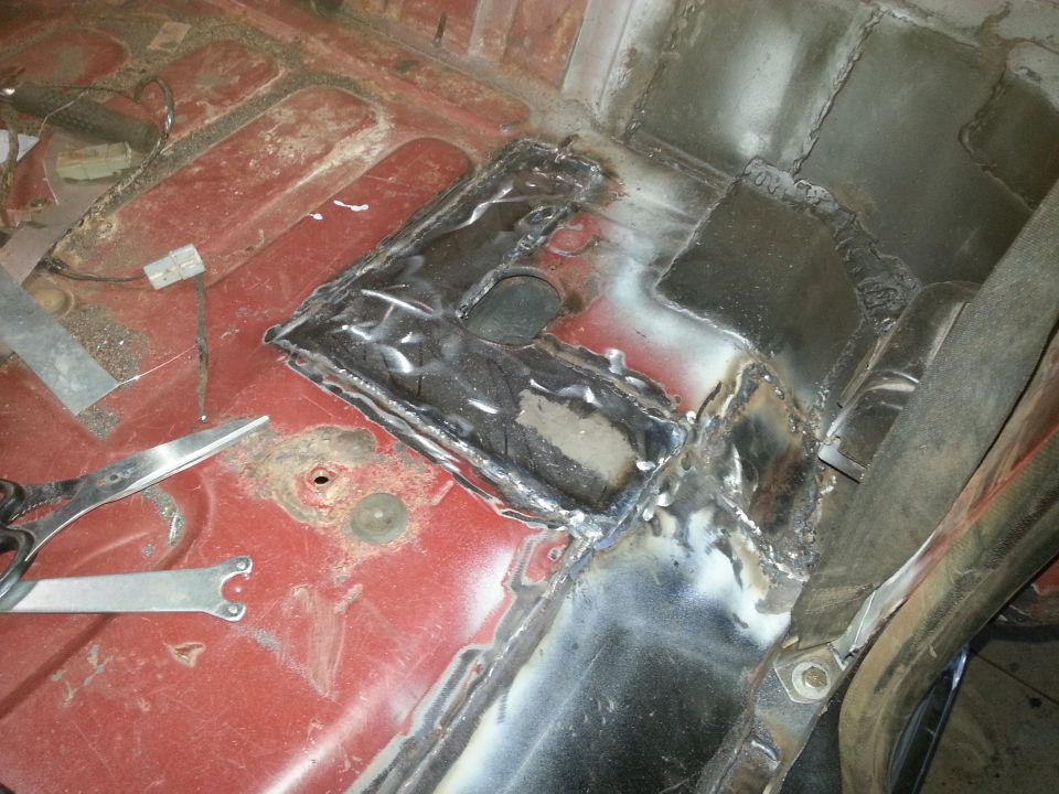 Welded metal patches on the red interior floor of a vehicle, with tools visible.