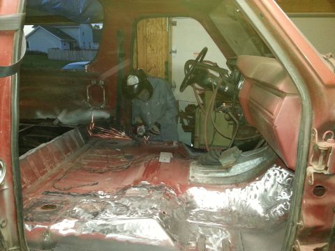 Interior view of a red vehicle being worked on, with sparks flying from grinding.