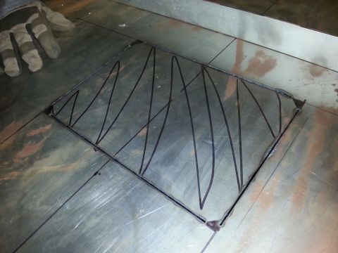 Gloved hand on metal surface with a metal frame and wire bracing.