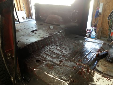 Interior floor of a vehicle undergoing restoration, showing exposed metal and cleaning supplies.