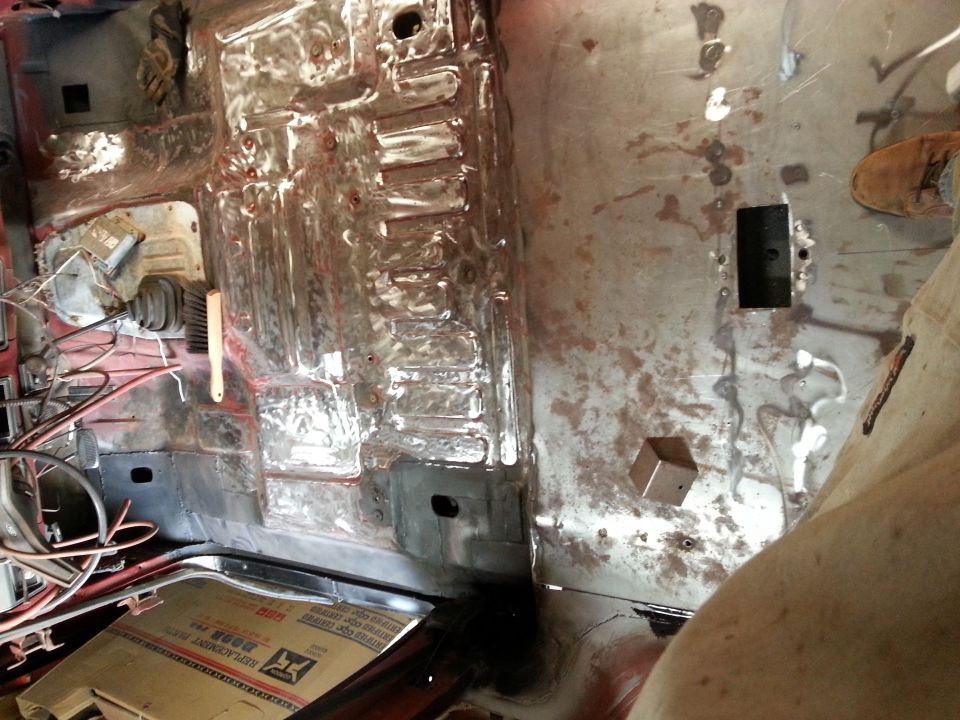 Bare metal interior of a vehicle with transmission tunnel, steering wheel, and replacement parts box.
