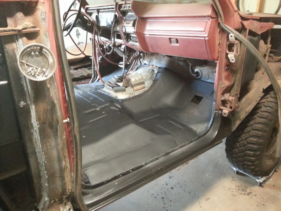 Interior of a classic Ford Bronco with driver's door open, showing floor pan, dashboard, and wiring.