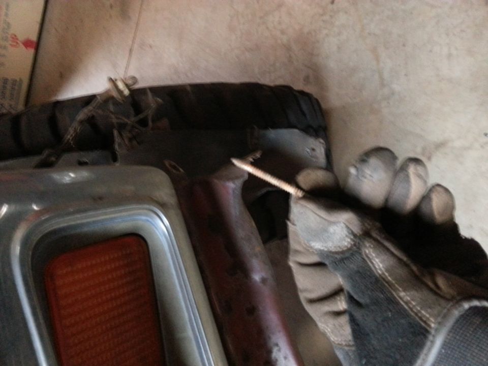 Gloved hand holding a screw near a vehicle part.