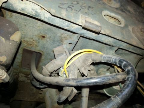 Close-up of vehicle wiring harness and rusty metal components under the hood.