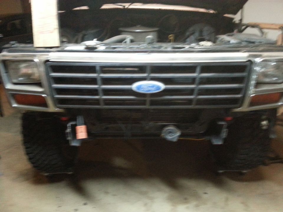 Front view of a classic Ford Bronco with hood open, showing grille and headlights.