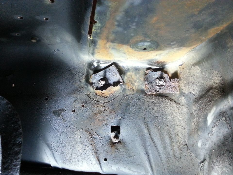 Close-up of rusted metal brackets and bolts on a vehicle undercarriage.