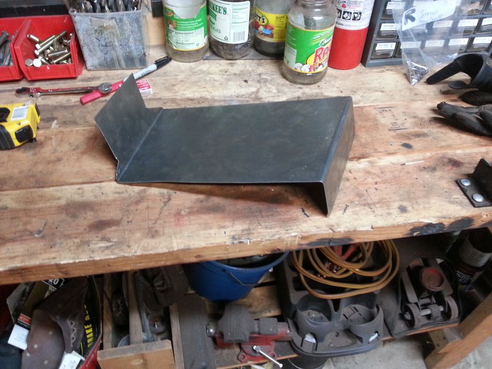 Metal bracket on a workbench with tools and supplies.