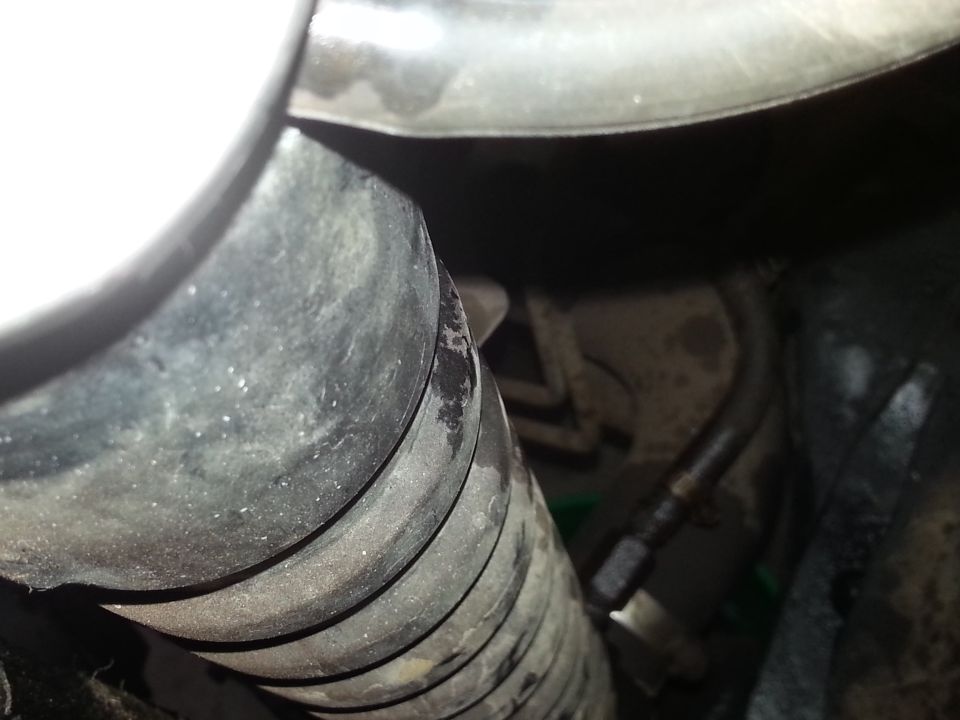Close-up of a black ribbed rubber hose with a metal fitting in a vehicle engine bay.