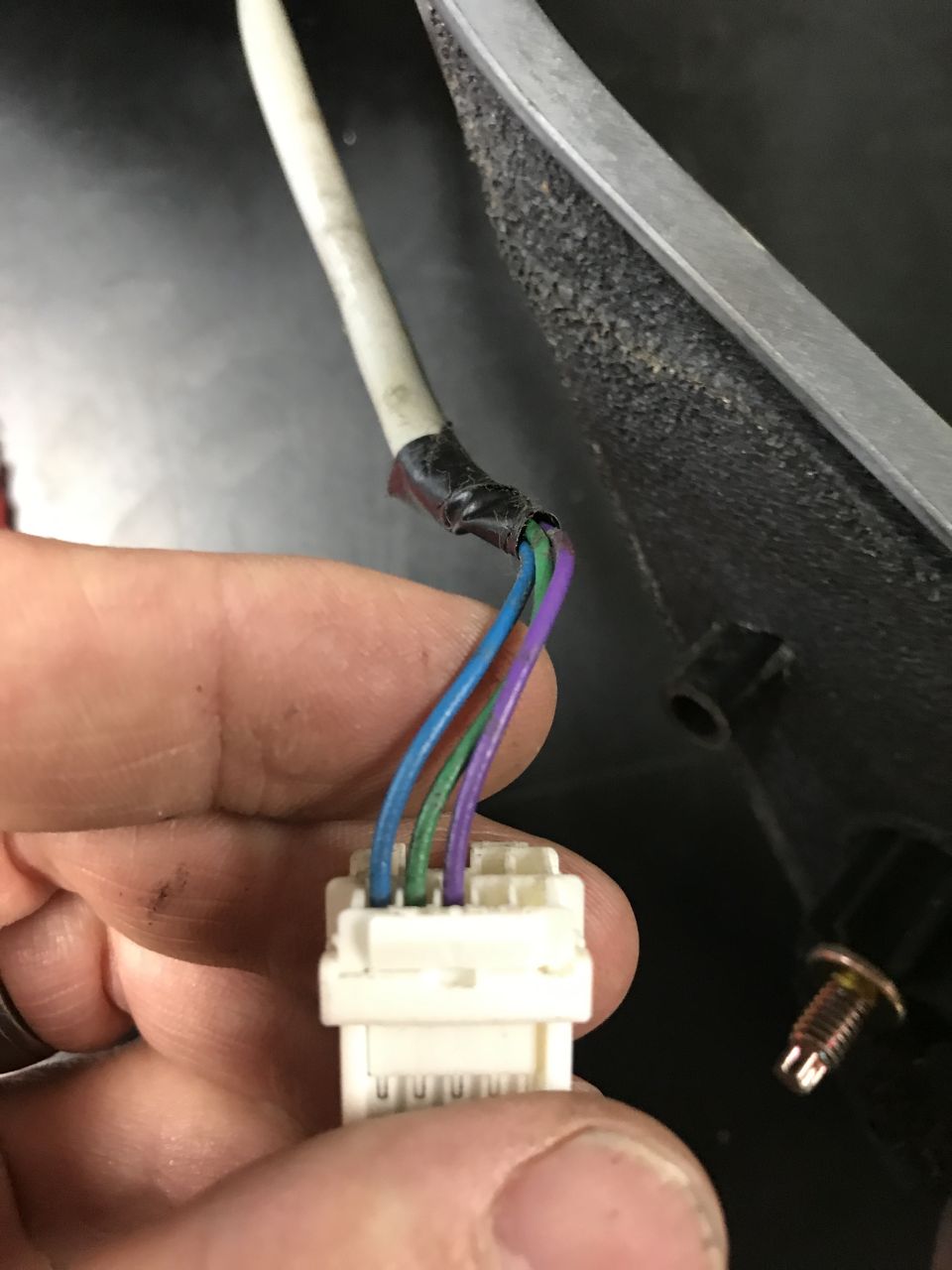 Close-up of a hand holding a white electrical connector with four wires: blue, green, purple, and one taped over.