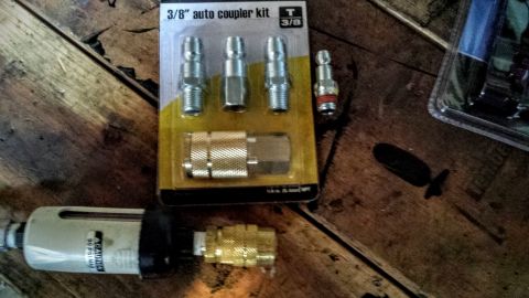 Air compressor accessories including a coupler kit and filter on a wooden surface.