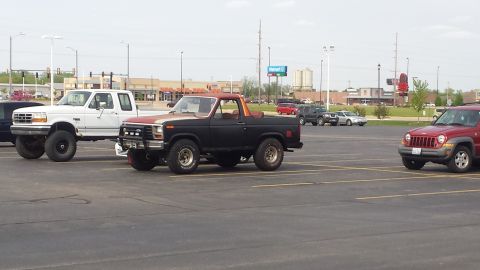 Black Ford Bronco and red Jeep Liberty parked in a lot, with a white Ford F-250 nearby.