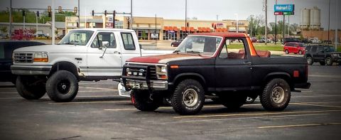 Black lifted Ford Bronco with red accents parked next to a lifted white Ford F-Series truck.