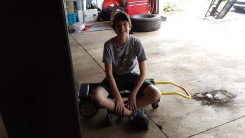 Young person sitting on a dolly in a garage.