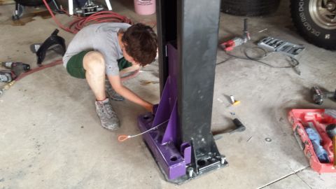 Person working on a car lift in a garage with tools and a tire visible.