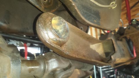 Rusty suspension arm with yellow bushing connected to differential housing of a 1984 Ford Bronco.