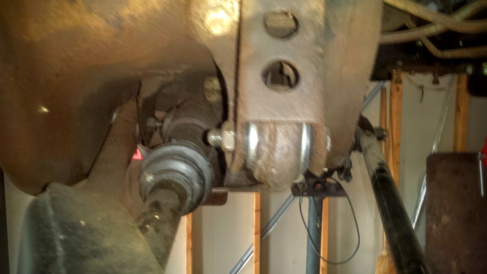 Underside view of vehicle suspension with rusty CV joint and drive shaft.