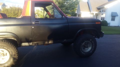 Side view of a dark Ford Bronco with a red roof and orange trim.