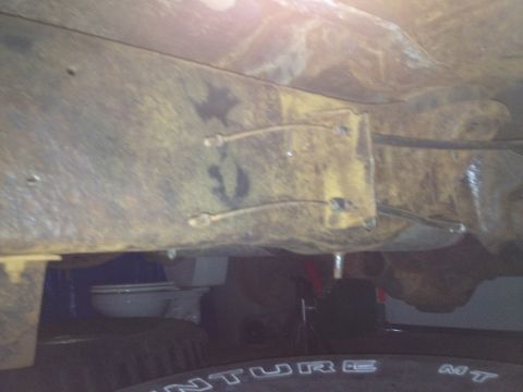 Underbody view of rusty frame rails and suspension parts, with a tire visible at the bottom