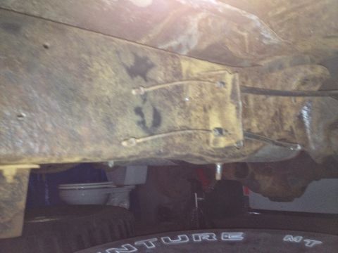 Underside of a vehicle frame with some rust and wiring. A toilet is visible underneath