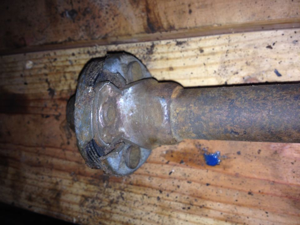 Close-up of a rusty driveshaft U-joint assembly on wooden planks