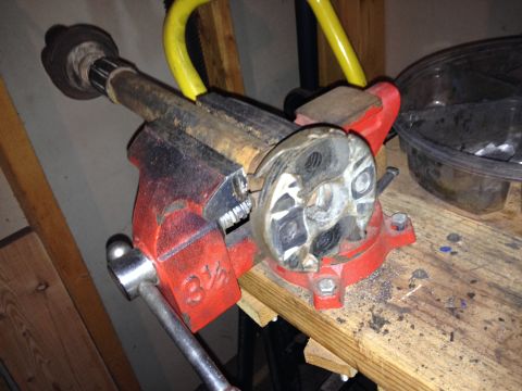 Red vise gripping a metal shaft with a fluted end, on a wooden workbench