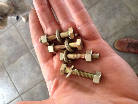 Hand holding four gold bolts with nuts and washers, one bolt has a bent washer