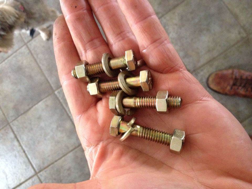 Hand holding four gold bolts with nuts and washers, one bolt has a bent washer