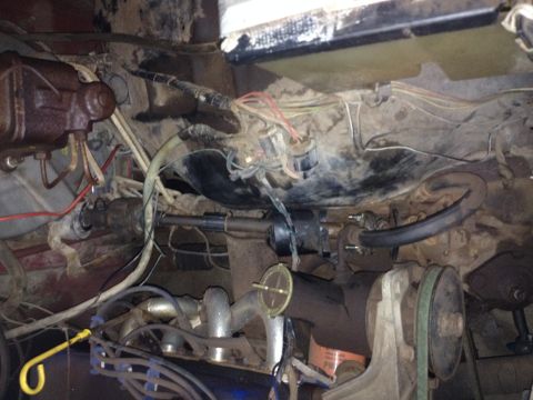 Engine bay with exposed wiring, hoses, and steering column. A yellow dipstick handle is visible