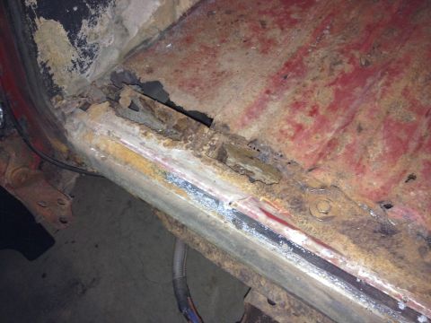 Close-up of heavily rusted metal frame and floor pan of a vehicle