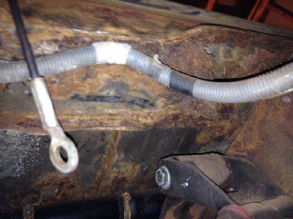 Rusted vehicle frame section with a corrugated wiring harness and a metal lug. A Supermotors.net watermark is visible
