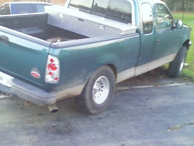 Rear passenger side of a dark green 1998 Ford F-150 pickup truck with a silver toolbox in the bed.