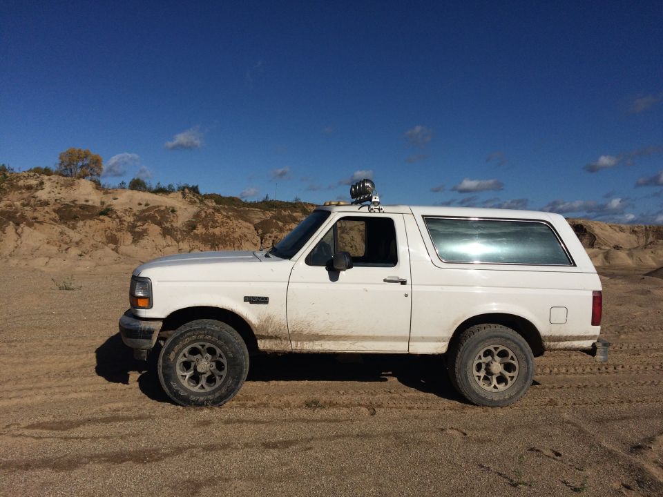 White Ford Bronco parked on sand, side view, with light bar on roof.