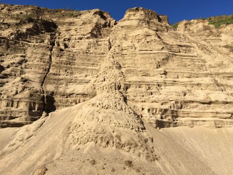 1993 Ford Bronco - A steep, eroded sand dune with visible layers of sediment and a clear blue sky above.