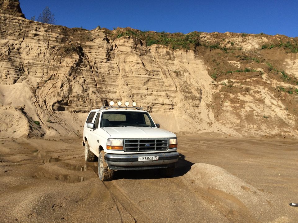 White Ford Bronco parked on sand with a large sand dune behind it.