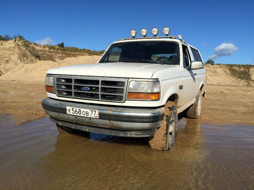 White 1993 Ford Bronco in mud and water with sand dunes.
