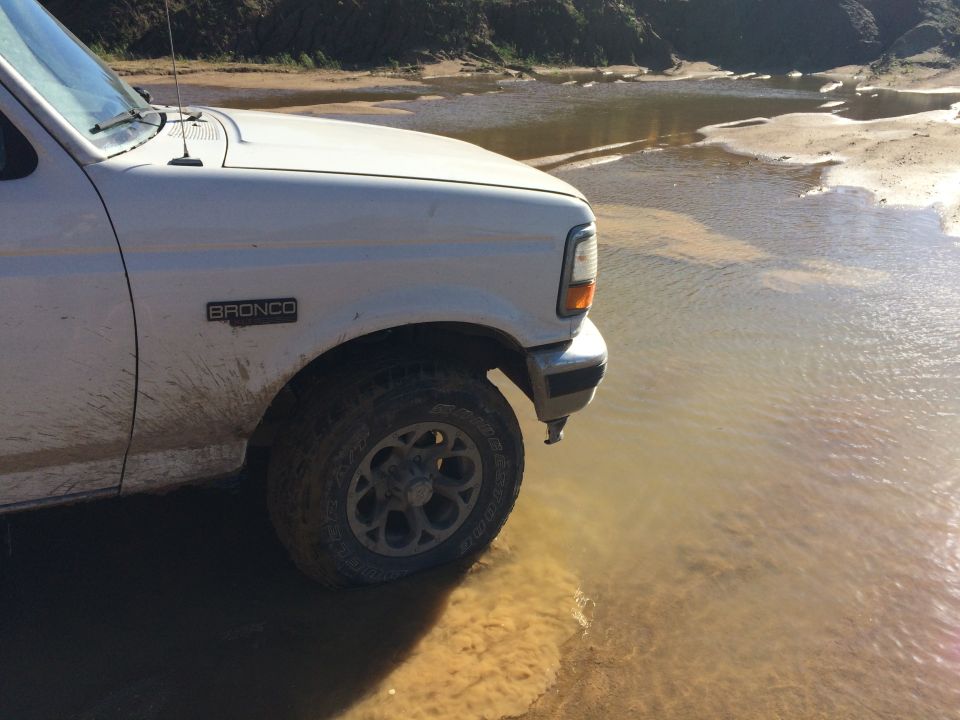 White Ford Bronco driving through shallow muddy water.