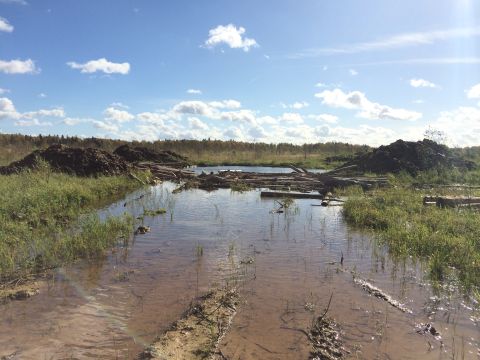 1993 Ford Bronco - A wide shot of a flooded area with logs and piles of dirt under a partly cloudy blue sky. The scene appears to be a construction or logging…