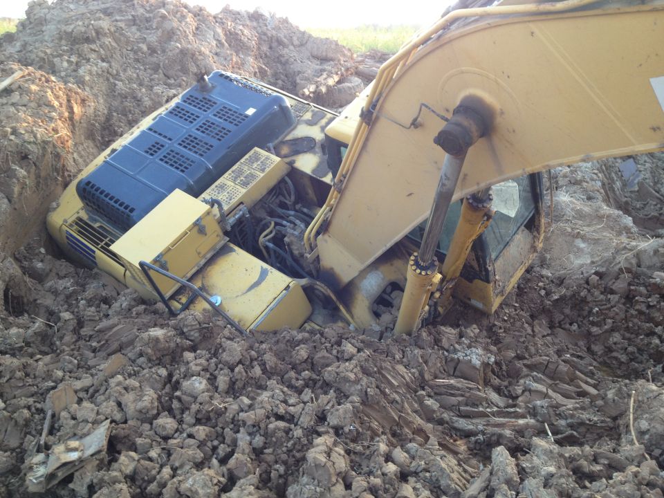 Yellow excavator stuck in a muddy trench.