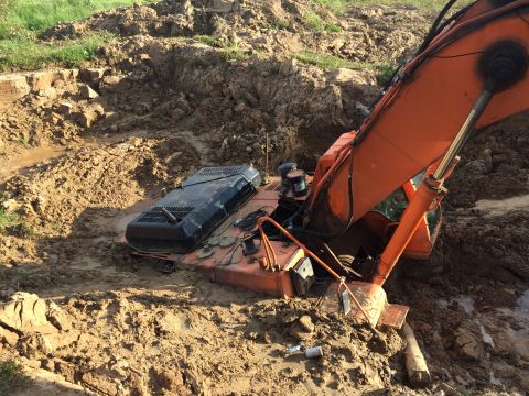 1993 Ford Bronco - An orange excavator is stuck in a muddy pit. The excavator's engine compartment is partially submerged in the mud and water.