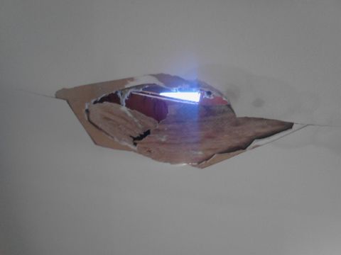 1989 Ford Bronco - A hole in a ceiling reveals insulation and a bright light source behind it.