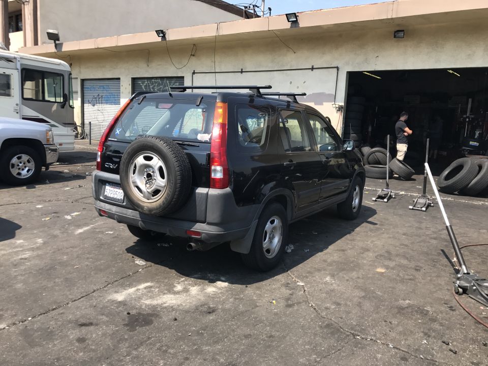 Black 2003 Honda CR-V with spare tire on rear door and roof rack parked outside a tire shop.