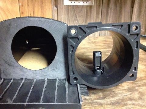 1996 Ford Bronco - Two black plastic automotive intake components are shown side-by-side on a wooden surface. The component on the left has a large circular o…