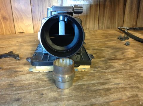 1996 Ford Bronco - A black mass airflow sensor housing is shown on a wooden surface, with a metal socket in the foreground. The mass airflow sensor housing ap…