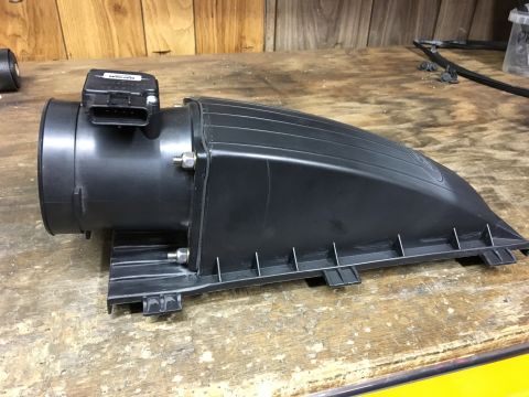 1996 Ford Bronco - A black plastic mass air flow sensor housing with a connector is shown resting on a wooden workbench.