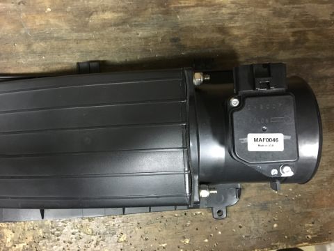 1996 Ford Bronco - A black mass air flow sensor (MAF) with a label reading "MAF0046 Made in USA" is attached to a black plastic air intake tube. The part is r…