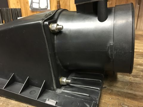 1996 Ford Bronco - A close-up view of a black plastic air intake box with visible bolts and nuts, mounted on a wooden surface.