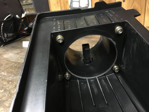 1996 Ford Bronco - A close-up view of the interior of a black plastic air intake housing, showing several hex screws securing a circular flange with a black p…