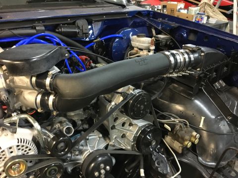 1996 Ford Bronco - Close-up view of a modified engine bay in a blue 1996 Ford Bronco, featuring a large black intake tube with K&N branding and various hoses…